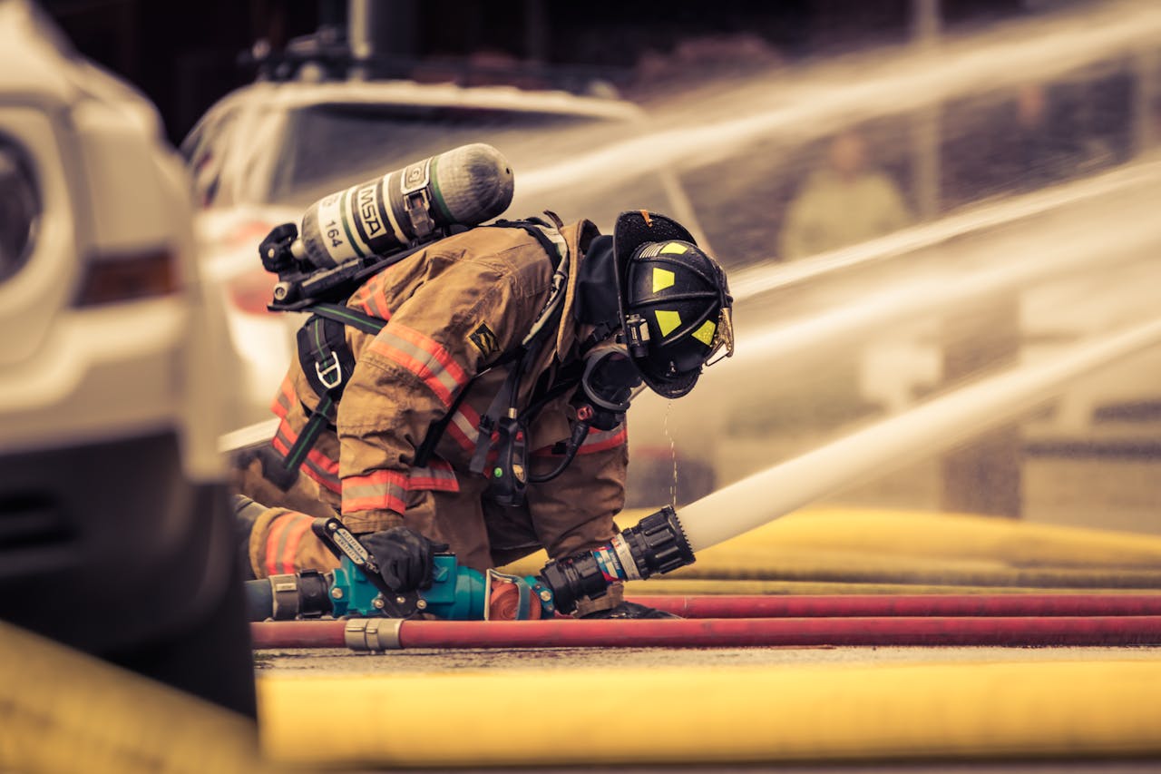 Firefighter in full gear handling water hose during emergency response training outdoors.